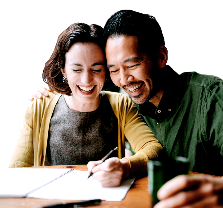 husband and wife sitting at a table with an open notebook and laughing